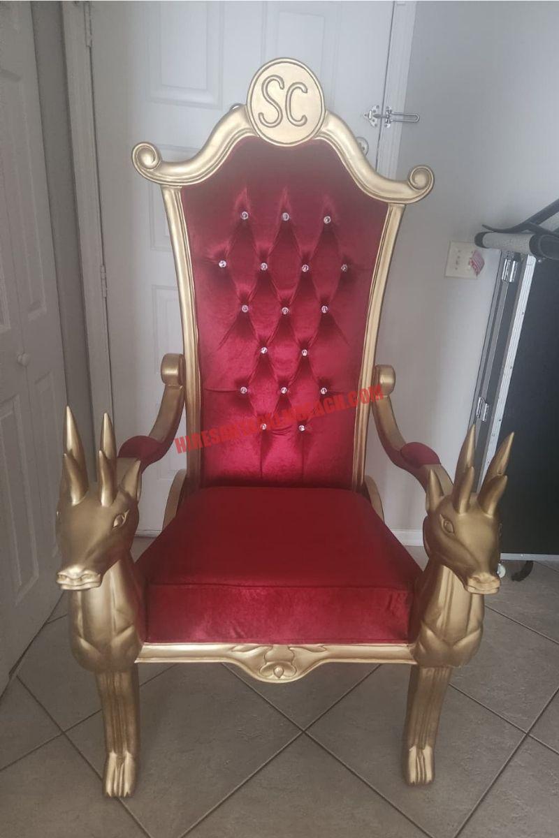 Empty gold Santa chair with a red tufted back and reindeer armrests on beige tile, no Santa.